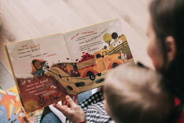 Adult reading a colorful picture book to a young child.