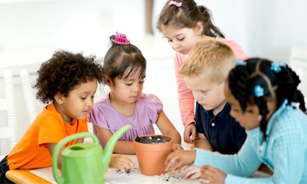 A group of young students, preschool and kindergarten, sit together planting seeds.