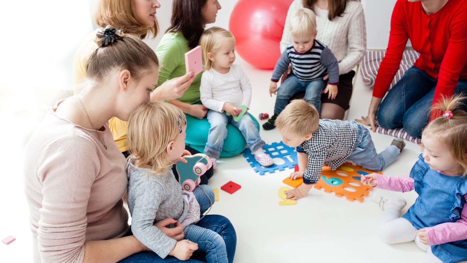 Parent and child playgroup interact in a circle on the floor.