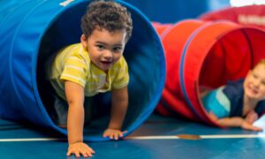 Toddler-age boy climbing through tunnel in care setting.