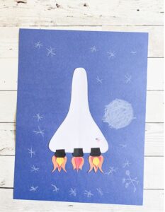 A construction paper craft of a white rocket on a blue background.