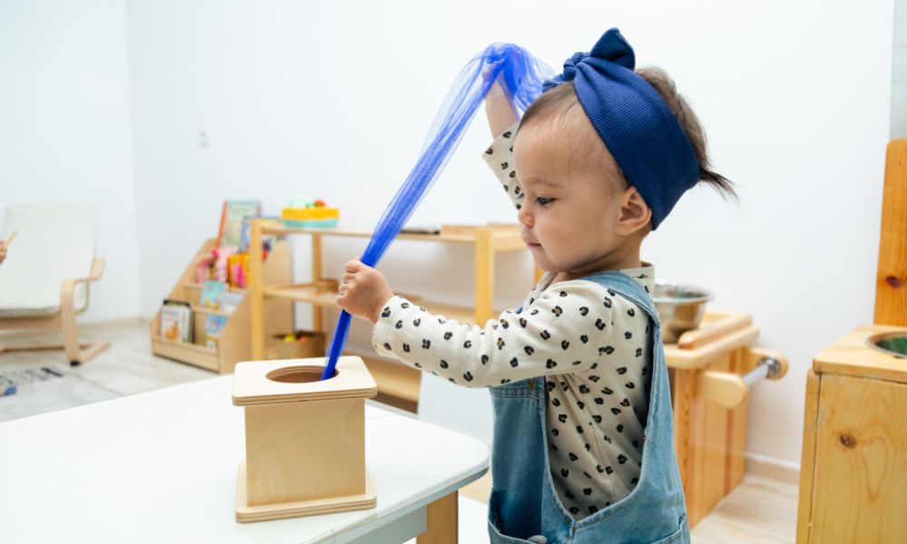 Toddler age girl pulls a purple ribbon out of a wooden box.