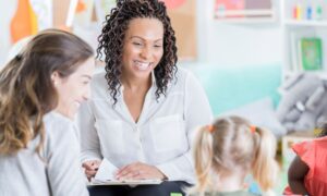 A teacher sits with a parent and toddler age child for a conference.