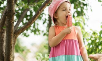 a young girl eats a red popsicle on a sunny day.