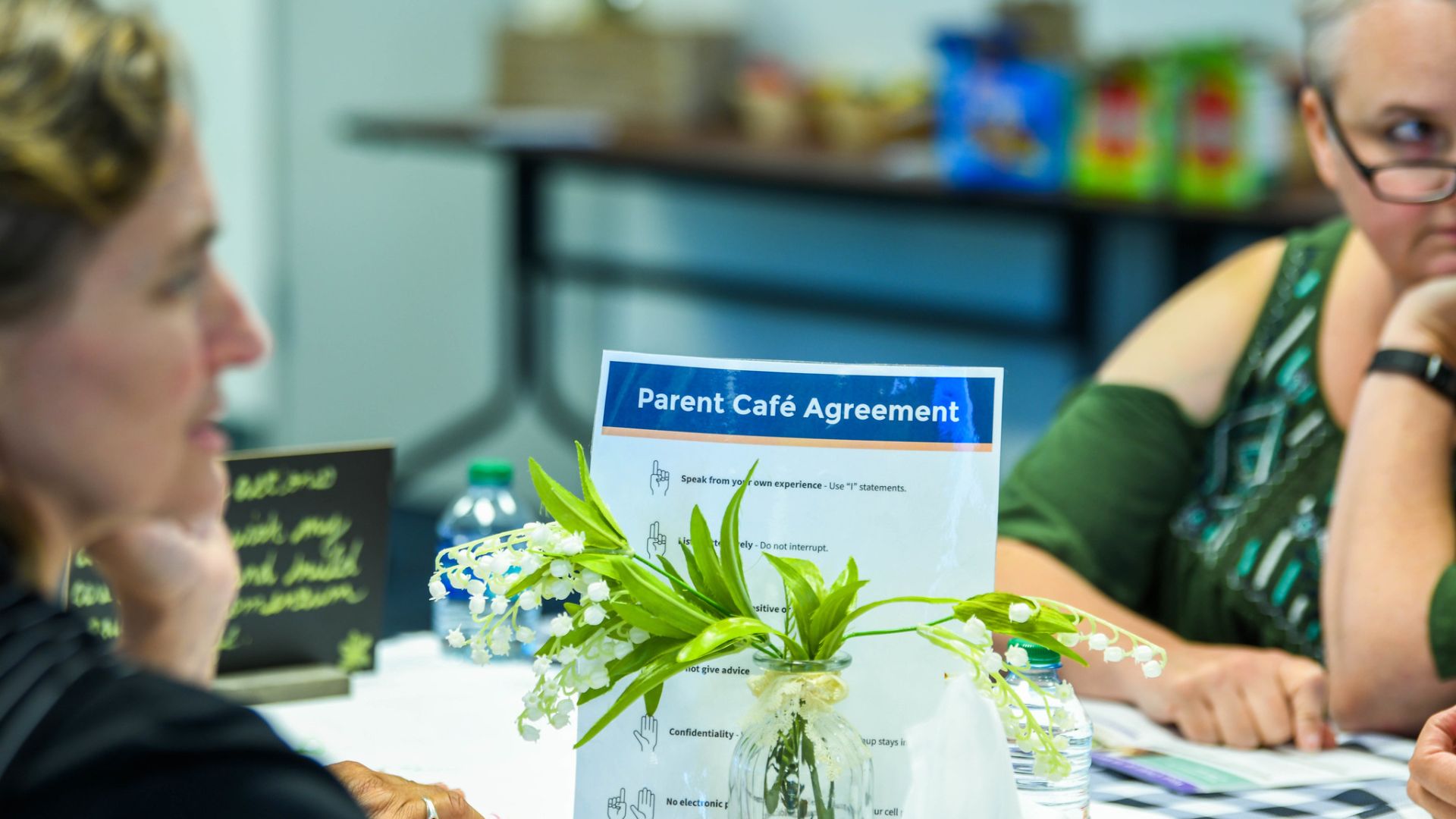 Photo of attendees of a parent café - two adults sit at a table to talk,