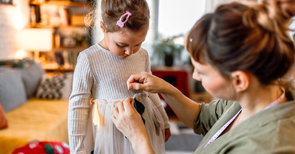 mom and daughter work on an autumn activity - decorating a dress to make a homemade costume.