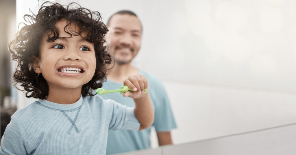 Brushing teeth, kid and boy with dental hygiene with father as child development in the bathroom for health and care. Young, mockup and toddler cleaning his oral or mouth in the mirror with dad