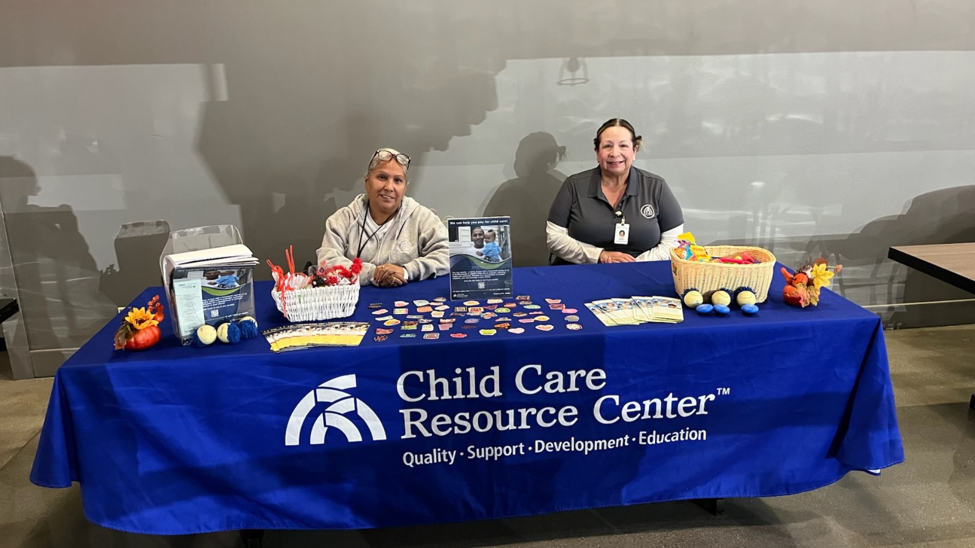 Two adults sit at a resource table handing out flyers and materials.